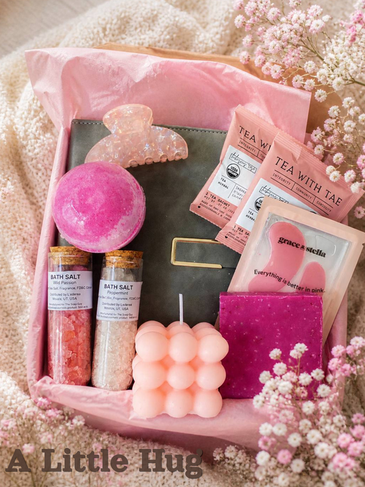 Soft pink self care gift box with bath salts, bath bomb, bubble candle, tea sachets, notebook, hair claw clip and cozy spa essentials surrounded by delicate baby’s breath flowers. Perfect relaxing gift for her by Lederea US
