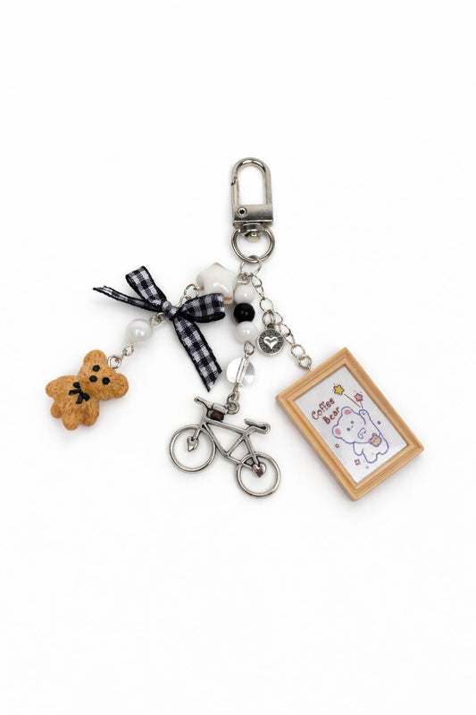 Keychain with various charms including a teddy bear, bicycle, and photo frame on a white background
